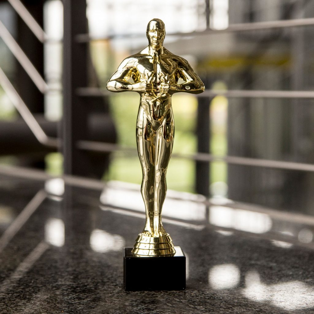 Goldene Figur ähnlich dem Hollywood Oscar auf Steinboden, im Hintergrund abgesoftet Bürogeländer