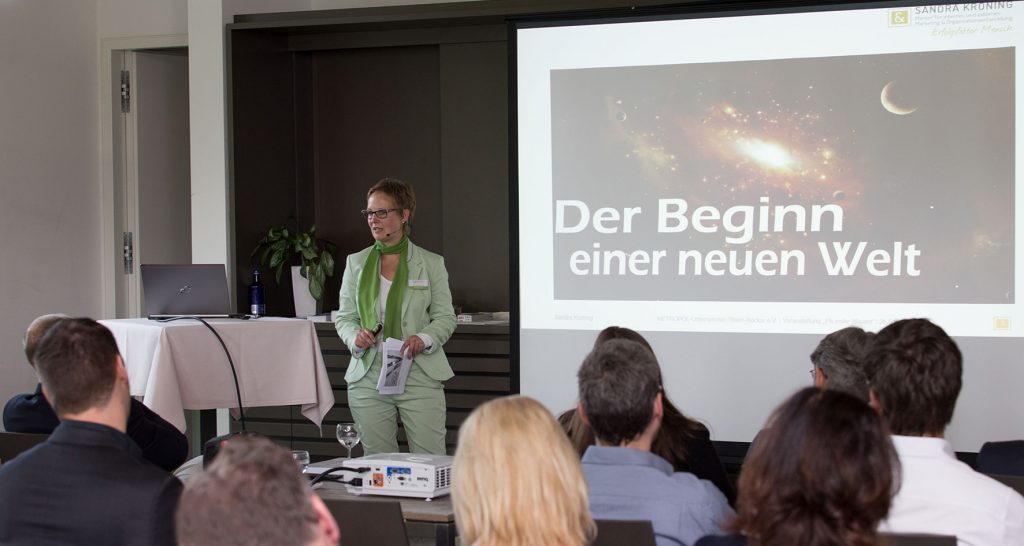 Sandra Kroning als Rednerin vor Gruppe, Businesskontext mit großer Leinwand